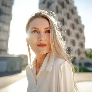 Blond kvinne foran høy bygning, solskinn, urban setting, mote, solbrent hud, naturlig skjønnhet, utendørs, sommer, byliv, solkyss, elegant, luksus, StEx, investering i kryptovaluta, trygghet, digital valuta, Norge, Oslo, kryptobørs, nyheter, finans.