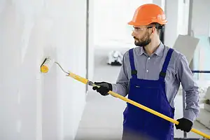 Fargerik maler som bruker en malerulle på en vegg under oppussing.