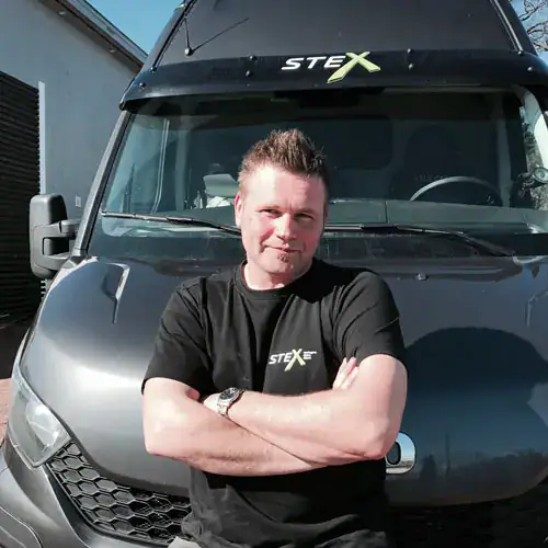 Modig mann foran STEX varebil, innovativ logistikk og transportløsning, profesjonell frakttjeneste, effektiv og pålitelig distribusjon, forretningsdrivende i Norge.
